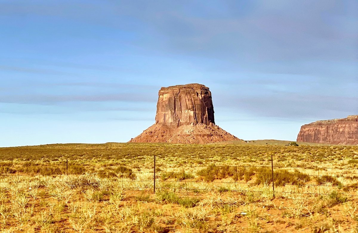 A long straight highway through Monument Valley, red rock buttes against a blue sky